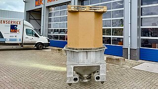 A cylindrical container stands upright in a metallic holder in front of a workshop