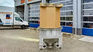 A cylindrical container stands upright in a metallic holder in front of a workshop