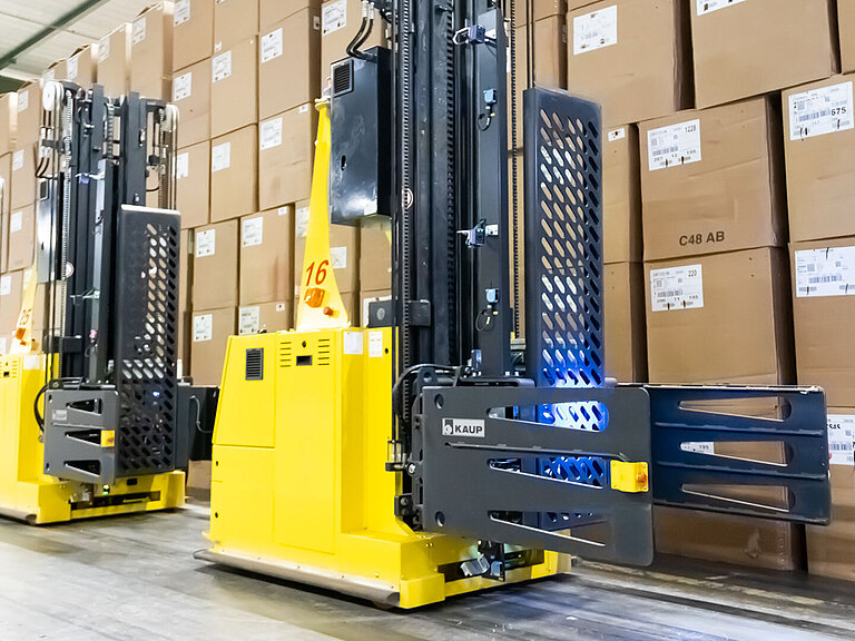 Two yellow driverless forklifts in front of a large number of stacked cardboard boxes