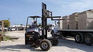 Petit chariot élévateur avec fourche levée et un camion chargé de pierres en arrière-plan