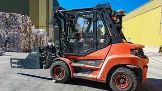 Seitenansicht einer roten Baumaschine mit Ballenklammer vor gepressten Altpapierballen