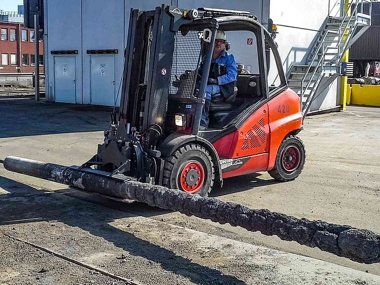 Un chariot élévateur rouge tient une lance à béton métallique dans une pince rotative spéciale