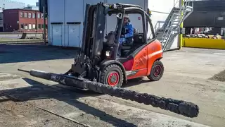 Ein roter Gabelstapler hält eine metallische Betonlanze in einer speziellen drehbaren Rollenklammer