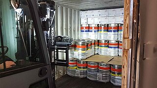 A forklift truck with a spotlight approaches several metal beer barrels in a container