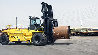 Un gros engin de chantier jaune transporte un rouleau de fil enroulé avec un eperon