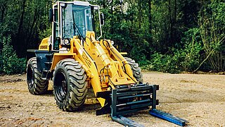 Excavadora amarilla sobre suelo arenoso con un accesorio de KAUP con el bosque de fondo