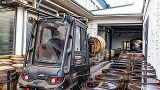 A forklift truck is manoeuvred through a narrow aisle with wooden barrels on both sides