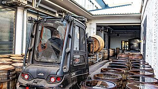 Un chariot élévateur est manœuvré dans un couloir étroit avec des fûts de bois de chaque côté