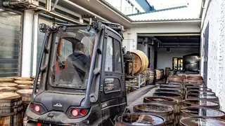 A forklift truck is manoeuvred through a narrow aisle with wooden barrels on both sides
