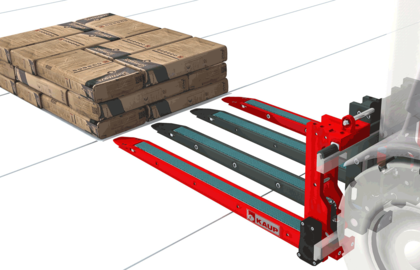 A stacker fork with four extendable tines drives towards a stack of packed building material