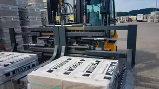A forklift truck with a special, wide double stone clamp transports packed stones