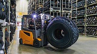 Una carretilla elevadora transporta verticalmente un neumático con una pinza de rodillos KAUP