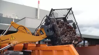 A construction machine dumps a box of rubble into an orange construction container
