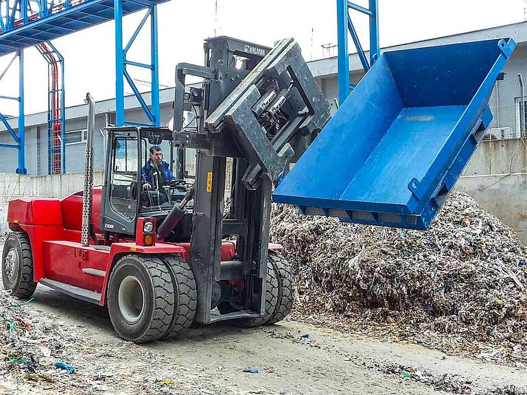 Una máquina con accesorio giratorio hace girar un contenedor de residuos de construcción azul