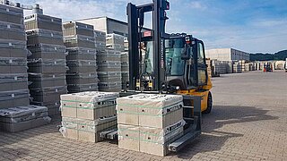 A yellow construction machine transports two stone packs with the help of a special attachment