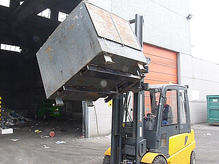 Una carretilla elevadora levanta una caja metálica y la hace girar frente a la puerta de un almacén