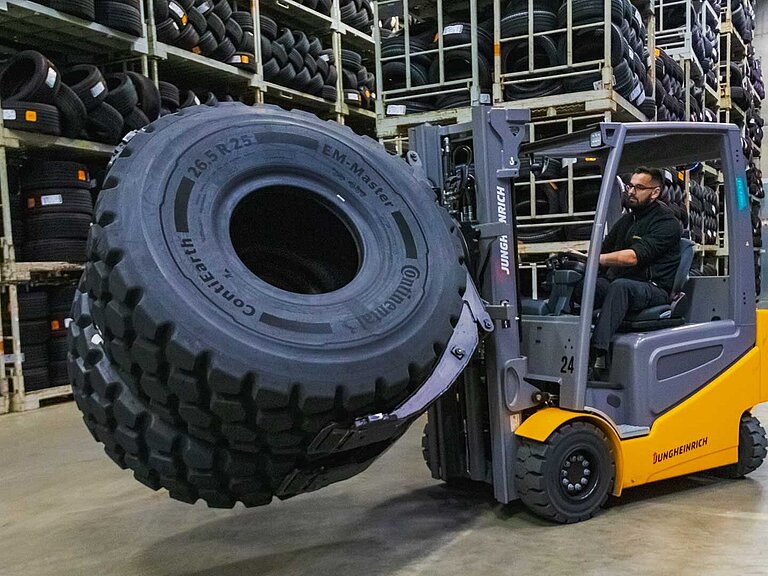 A yellow forklift truck transports two large tyres side by side with a tyre clamp