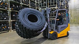 A yellow forklift truck transports two large tyres side by side with a tyre clamp