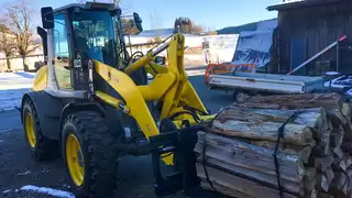 A yellow construction machine picks up several rolls of logs with a fork positioner