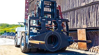 Eine große Baumaschine mit speziellem, drehbaren Anbaugerät manövriert über ein Bergbaugelände