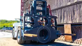 Eine große Baumaschine mit speziellem, drehbaren Anbaugerät manövriert über ein Bergbaugelände