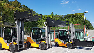 Three yellow forklifts with different clamp positions are parked in a row in an outdoor area