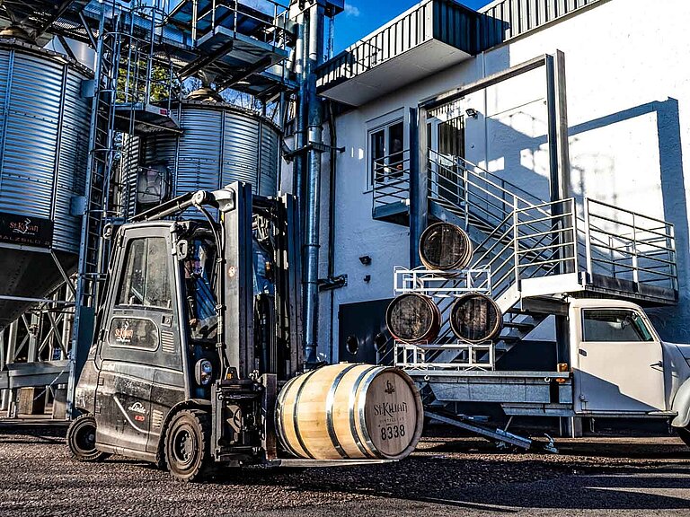 Una carretilla elevadora y una camioneta transportan barriles de madera de licor