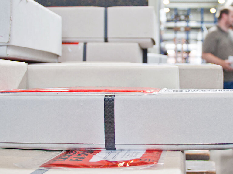 Elongated white parcels with red stickers are stacked on top of each other in a warehouse
