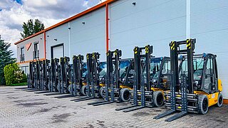 A fleet of yellow forklifts with identical attachments are lined up in a row