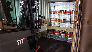 A forklift truck loads a container with beer kegs using a special attachment