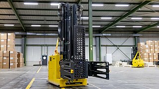 Front view of a yellow automated guided vehicle with a cardboard box clamp in a warehouse