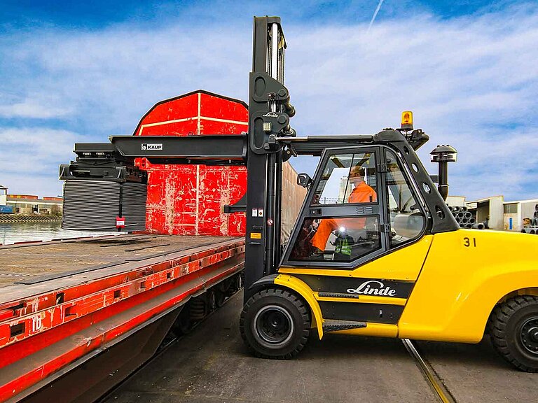 Eine gelbe Baumaschine platziert eine große Drahtrolle auf der Ladefläche eines Zugwagons