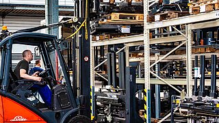 A forklift truck lifts a palletised spare part from the top shelf of a storage rack