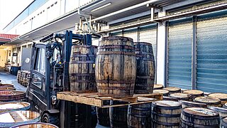 A forklift truck transports several wooden barrels on two pallets through a narrow aisle