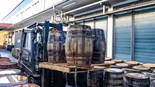 A forklift truck transports several wooden barrels on two pallets through a narrow aisle