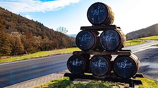 Five wooden whiskey barrels stacked into a pyramid stand by a roadside
