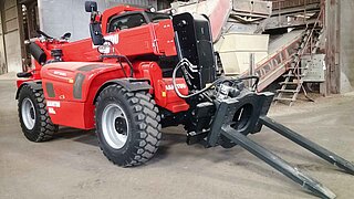 Engin de chantier rouge avec fourche rotative dont les pointes sont dirigées vers le sol