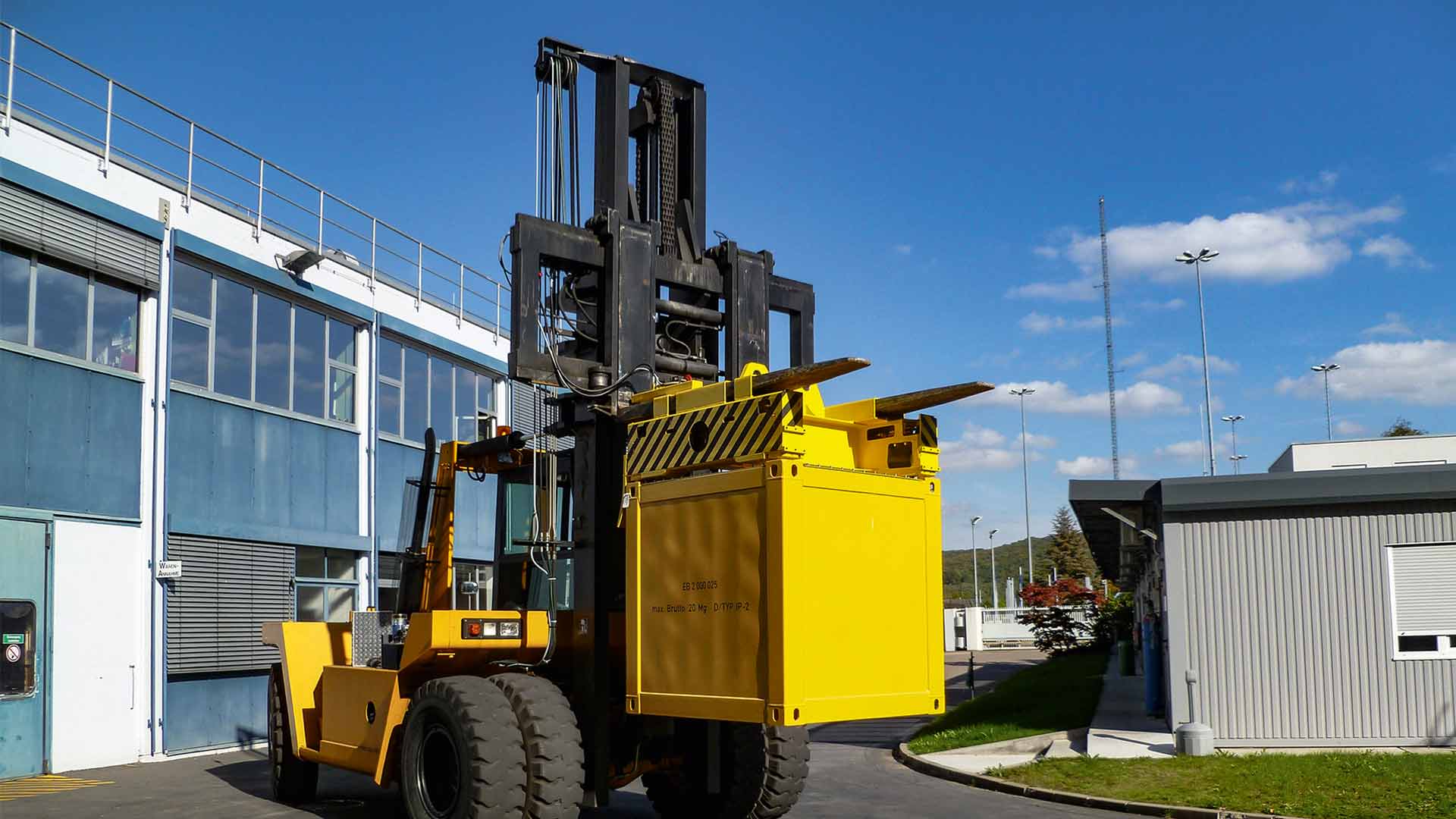 Yellow forklift truck with mounted container spreader and loaded square container