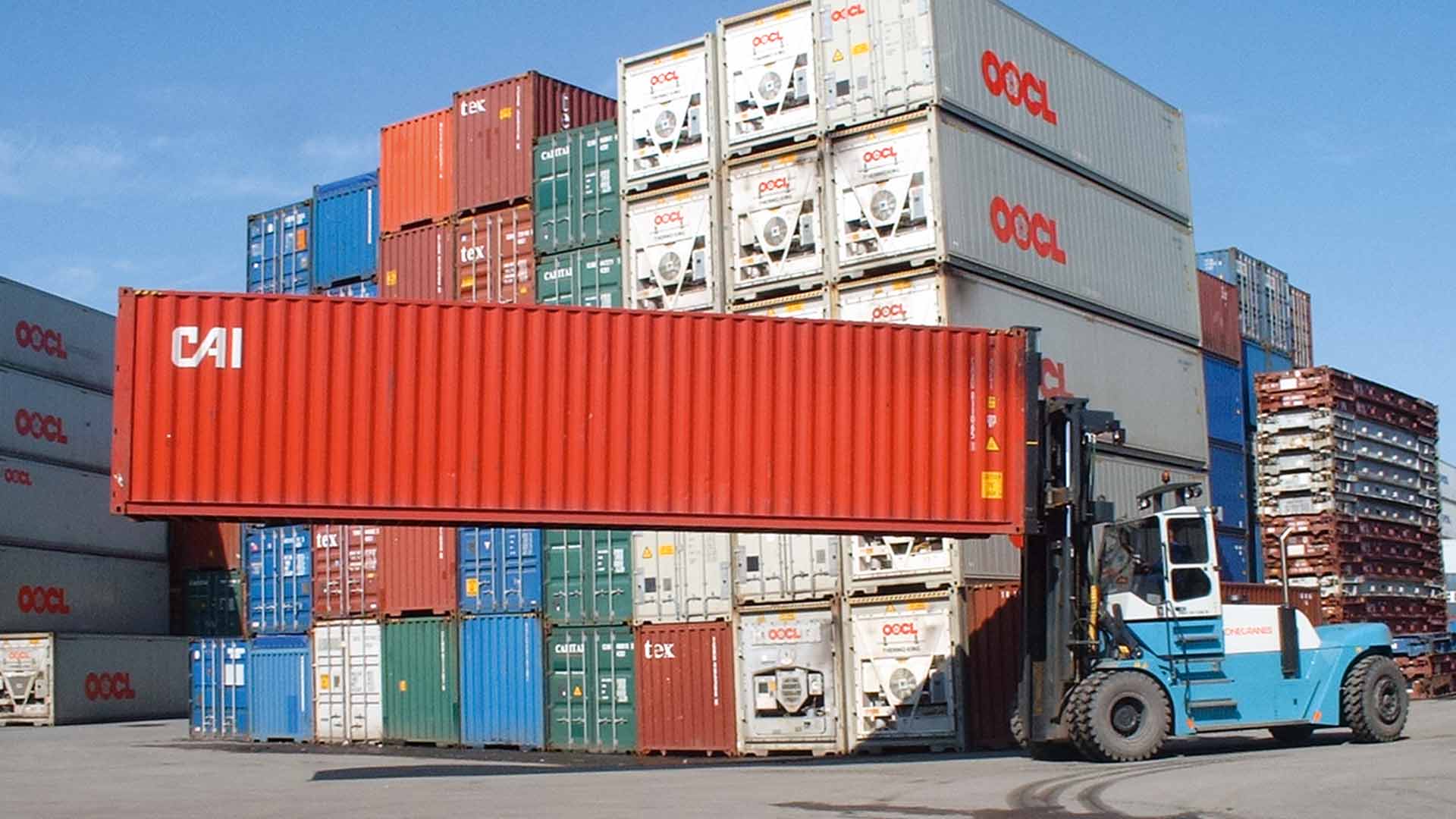 Ein Gabelstapler hebt einen roten Container an der Längsseite über einen Container-Lagerplatz