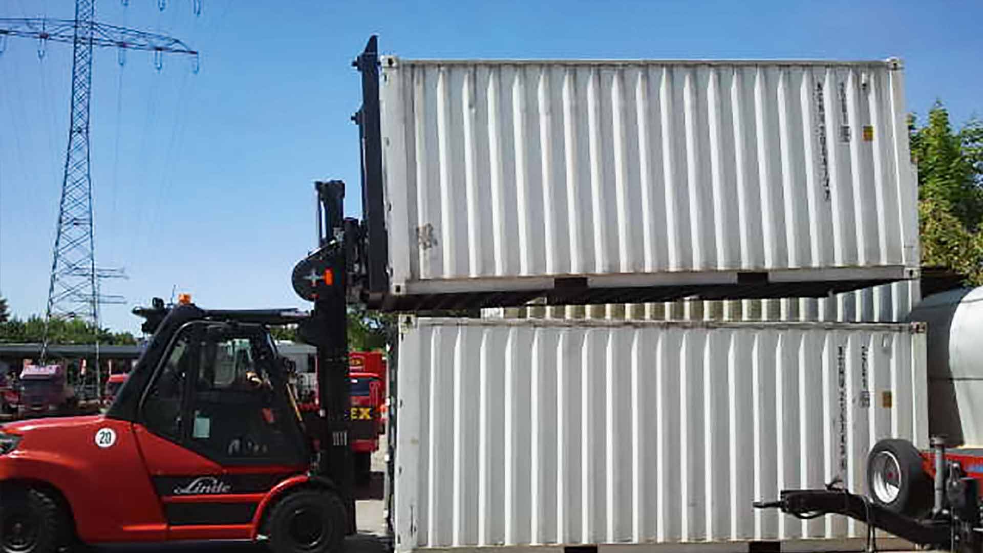 A red forklift truck lifts a container onto another container at the end face