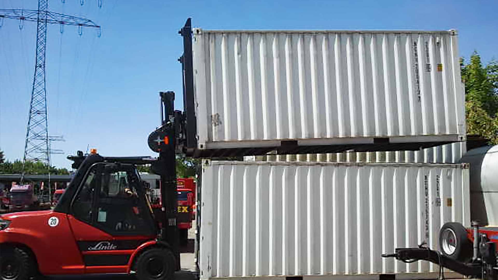 Ein roter Gabelstapler hebt einen Container an der Stirnseite auf einen anderen Container