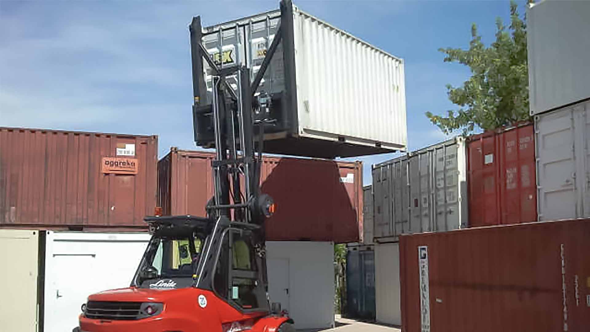 A red forklift lifts a container to place it on a stack of other containers