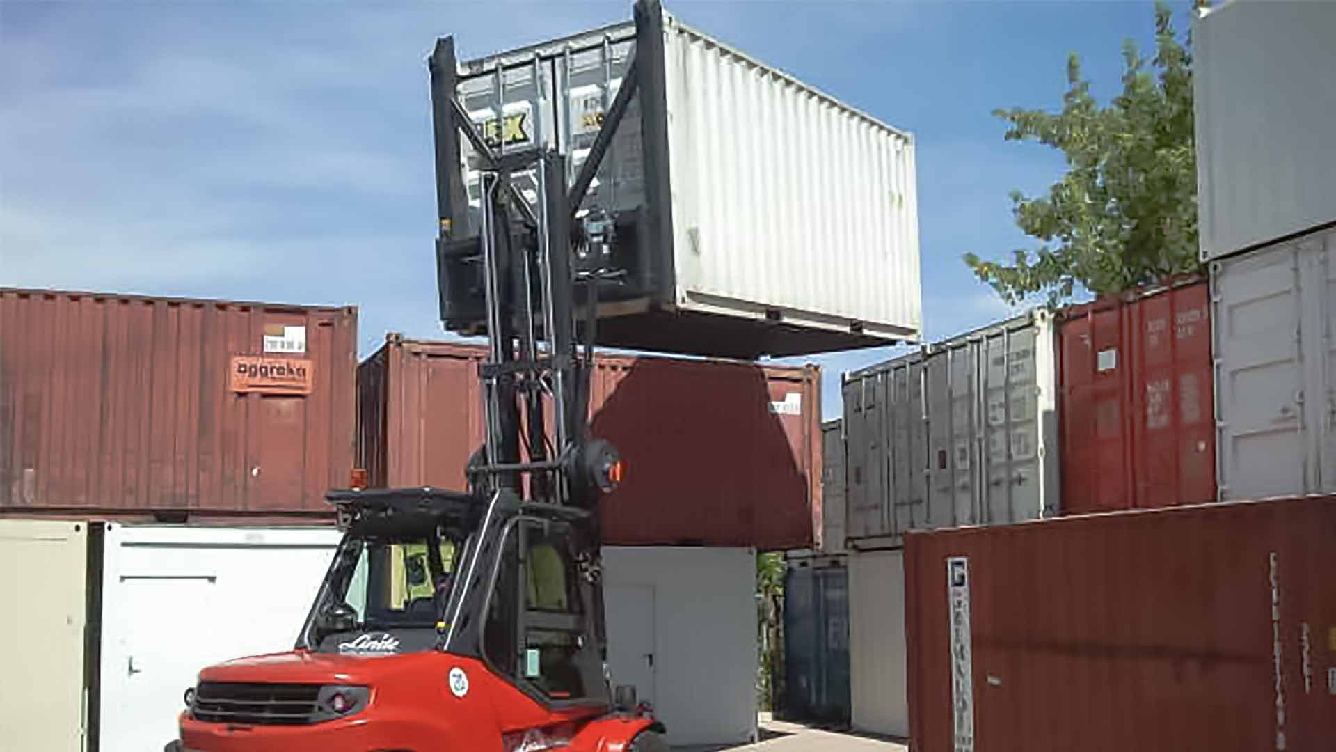 Un chariot élévateur rouge soulève un conteneur pour le placer sur une pile d'autres conteneurs