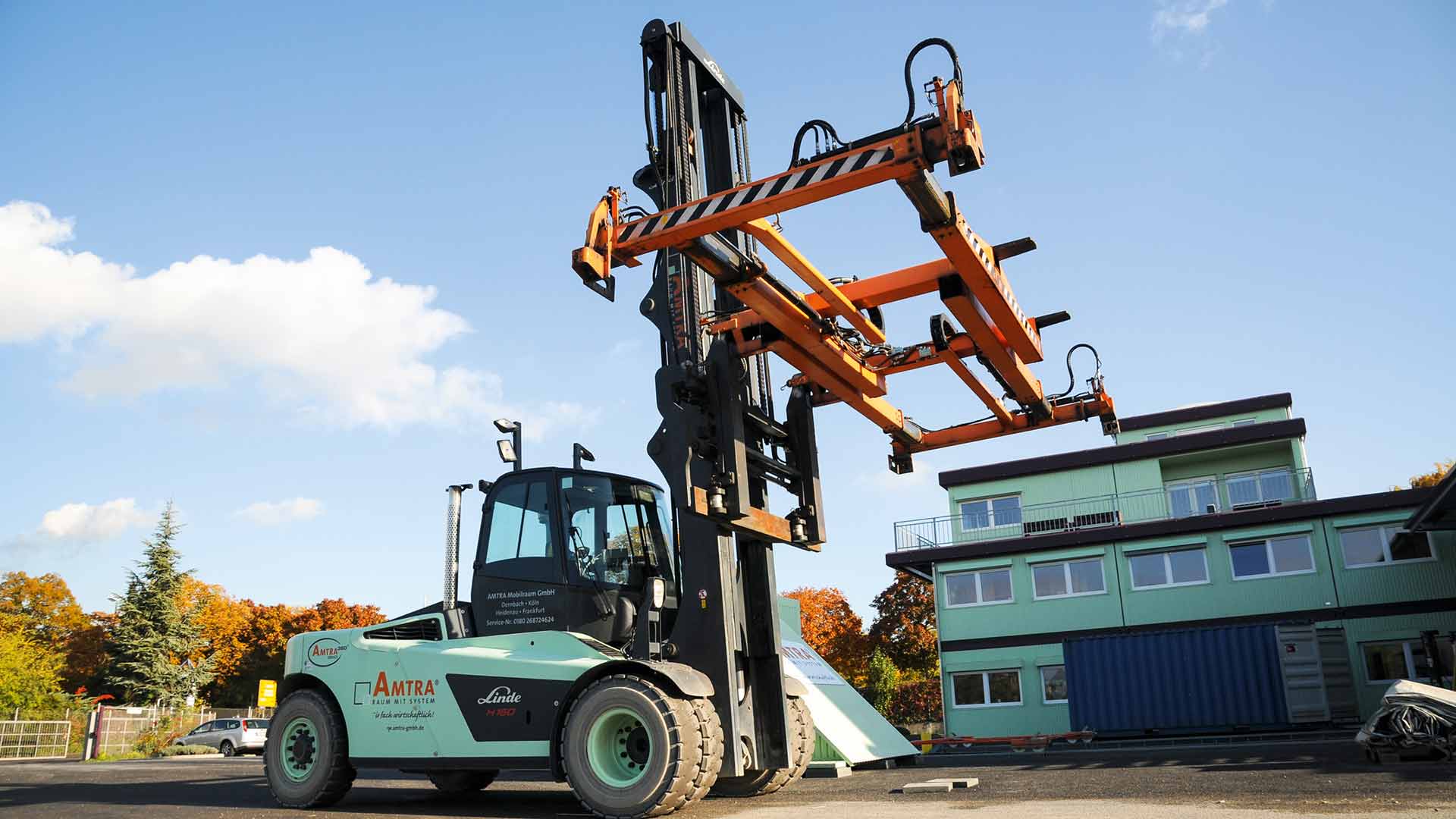 Eine Baumaschine mit orangefarbenem, ausgefahrenem Container Spreader auf einem Firmengelände