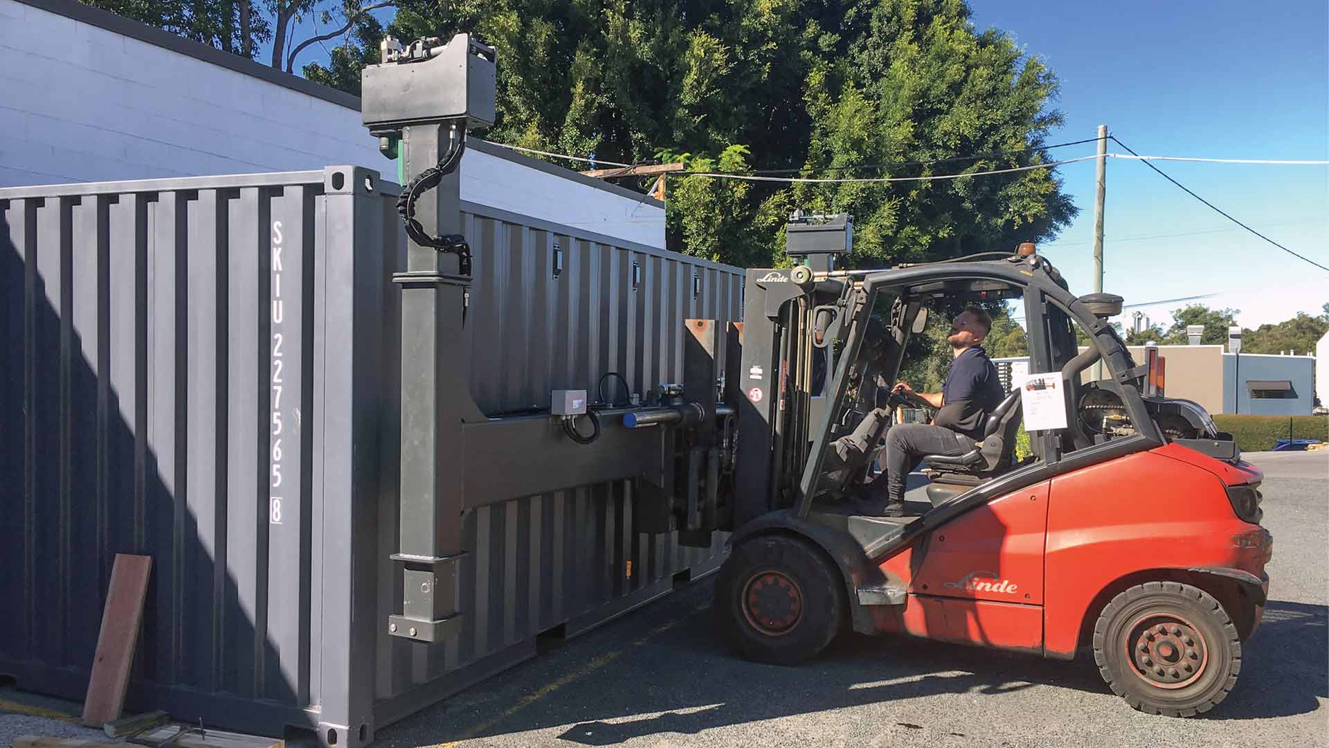 A red forklift truck equipped with a wide attachment picks up an empty container