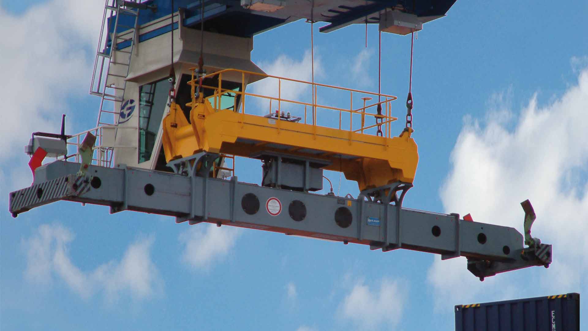 Crane arm with mounted container spreader from KAUP and operator's cabin in front of a cloudy sky