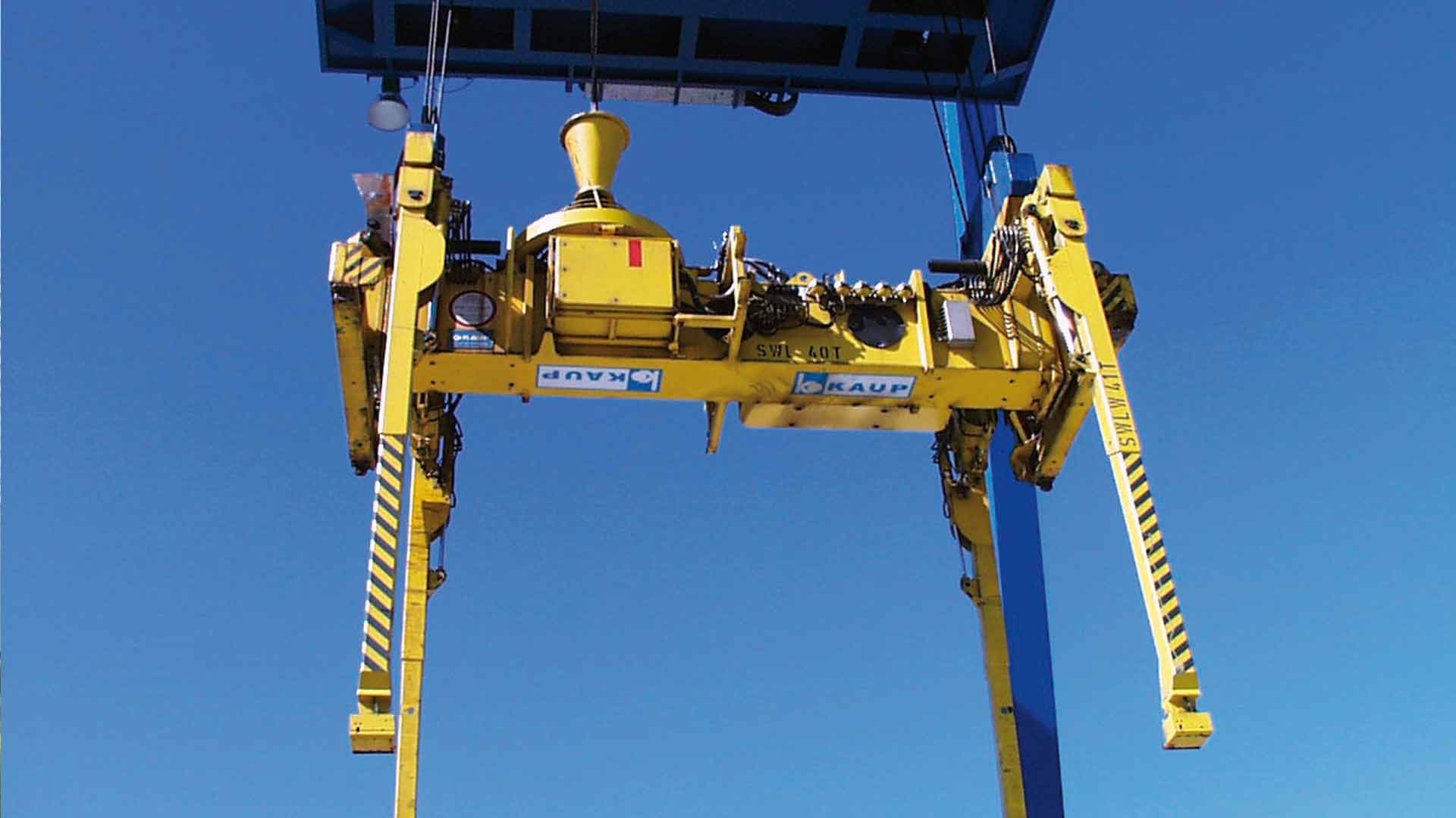 Grand spreader porte-conteneurs jaune Spreader de KAUP fixé à une grue devant un ciel bleu