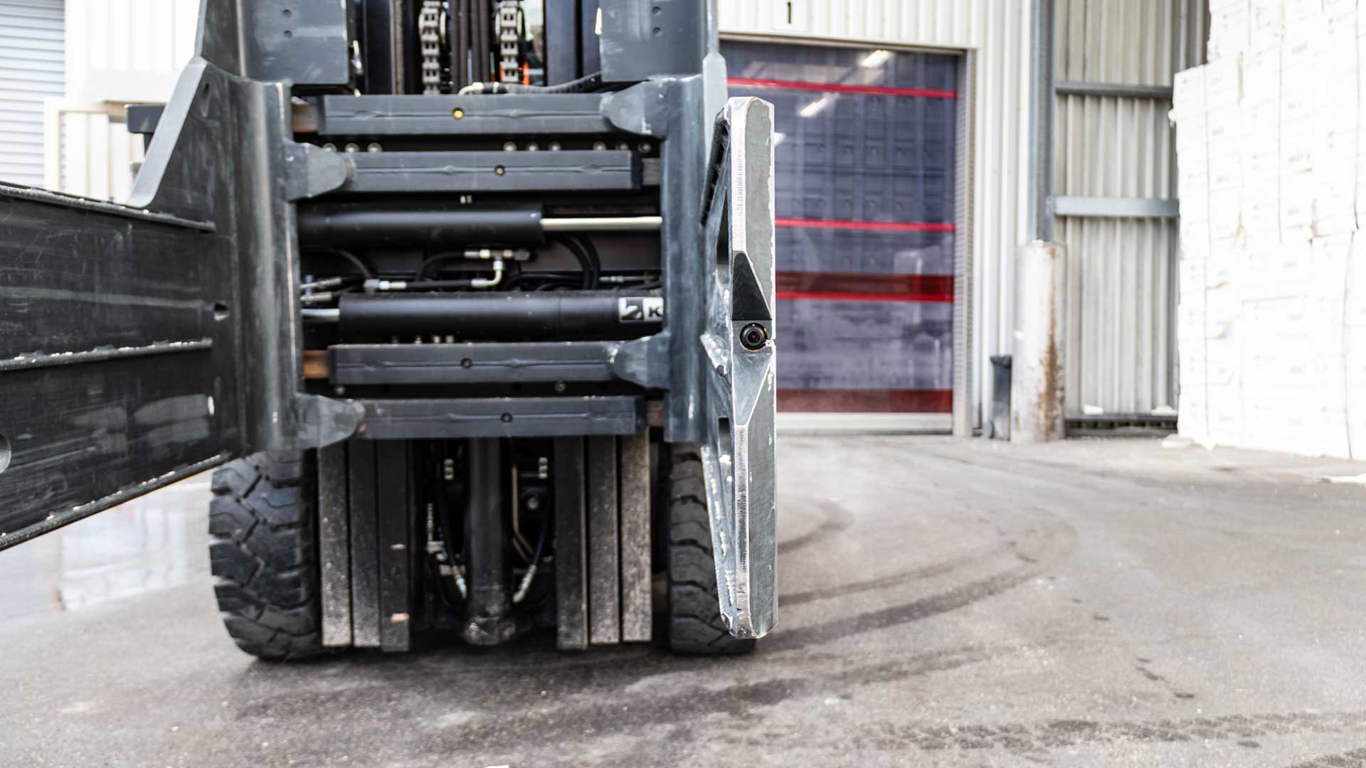 Lower part of a forklift truck with focused right clamp arm in front of a roller shutter door