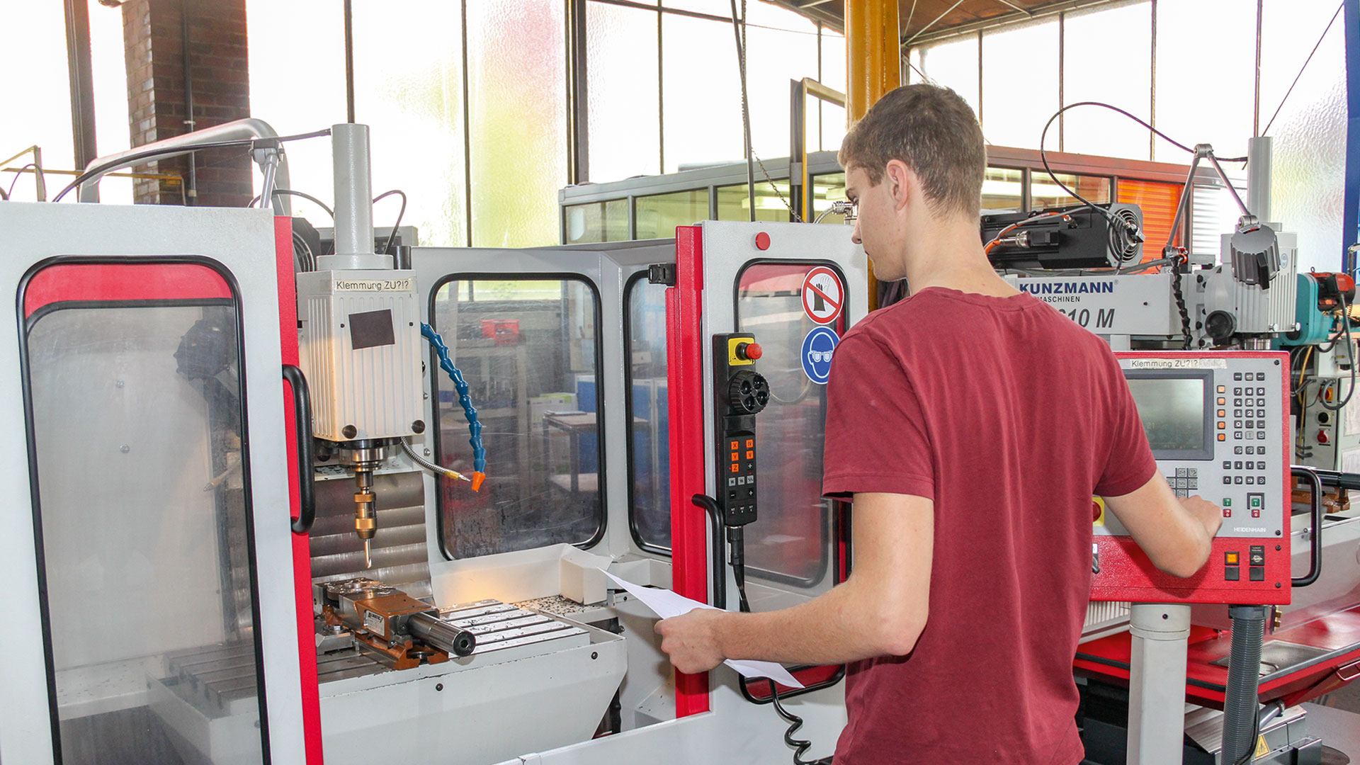 Rückansicht eines jungen Mannes in rotem T-Shirt bei der Bedienung einer Fräßmaschine