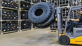 A forklift truck with rotating attachment lifts and transports two tyres through a warehouse
